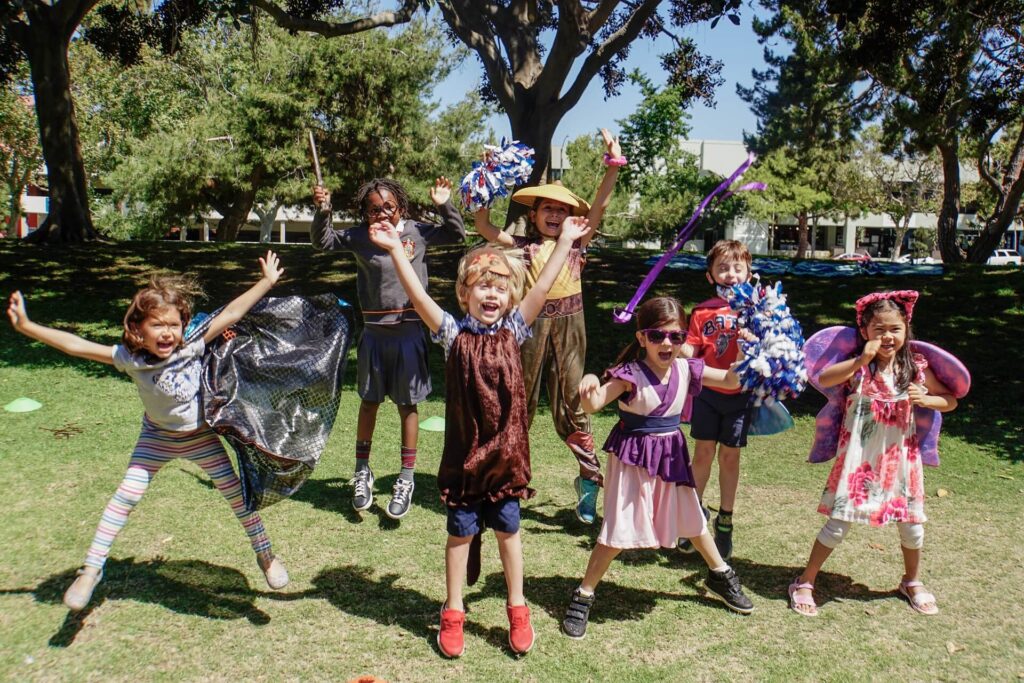 Kids On Stage children jump and play outdoors in colorful costumes during a summer theater camp activity.